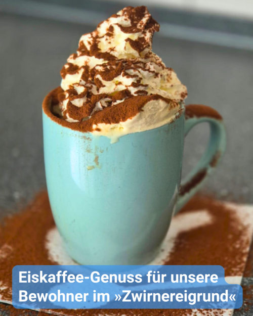 Eine hellblaue Kaffeetasse. Auf einem Kaffeeuntersetzer, bedeckt mit Kakaostreusel. Die Kaffeetasse hat eine Sahnehaube und Kakao oben drüber gestreut. Bildunterschrift: Eiskaffee-Genuss für unsere Bewohner im »Zwirnereigrund«